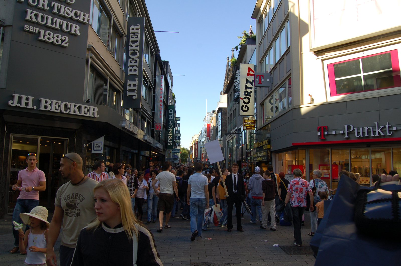 A man in a black suit with a blank white sign among shoppers on the Hohe Straße, Cologne